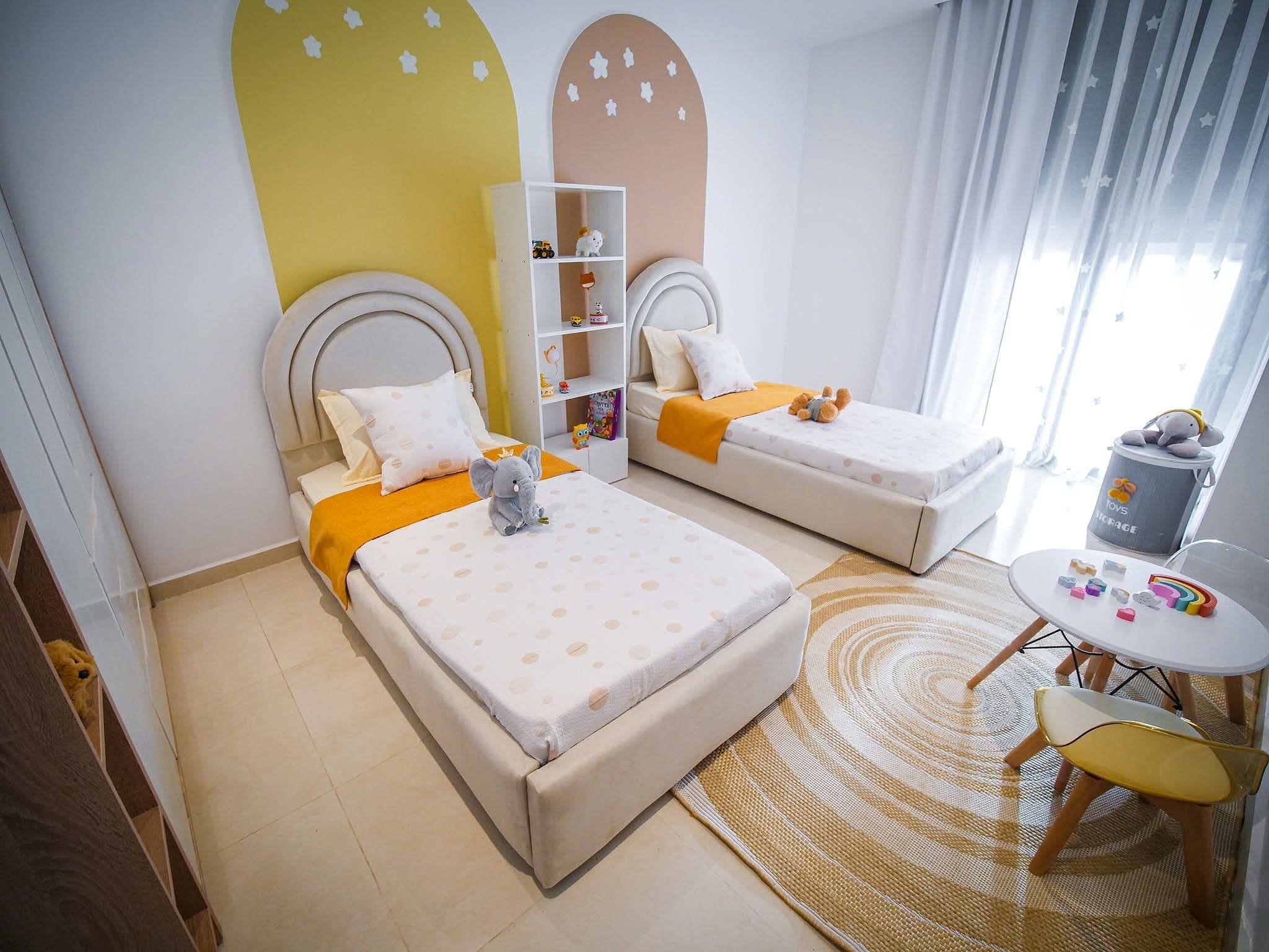 Chambre d'enfants avec deux lits, têtes de lit arrondies et décor coloré
